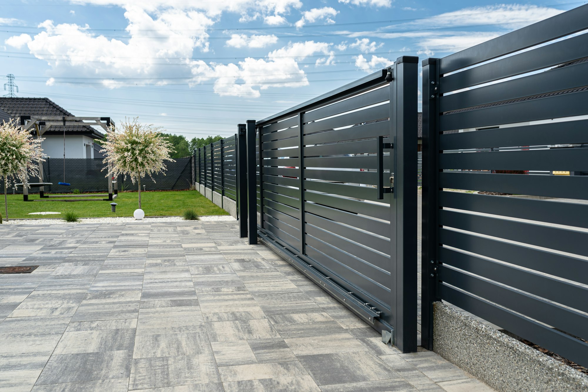 A modern panel fence in anthracite color, visible sliding gate to the garage and a slab driveway.